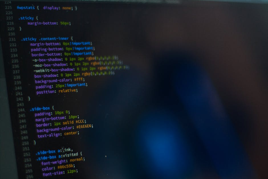 A detailed view of a computer screen displaying lines of colorful CSS code used for web design, with syntax highlighting in shades of yellow, blue, green, purple, and white on a dark background. The c