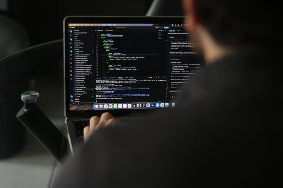 A person working on a laptop computer inside a vehicle, with the screen displaying lines of code in a dark-themed text editor. The individual's hand is visible on the laptop's keyboard, and the person